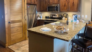 A kitchen with wooden cabinets, stainless steel appliances, granite countertops, and a glass display case with cookies.