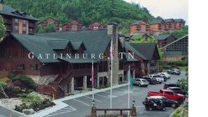 A lodge with a prominent entrance, a parking lot, and a mountainous backdrop.