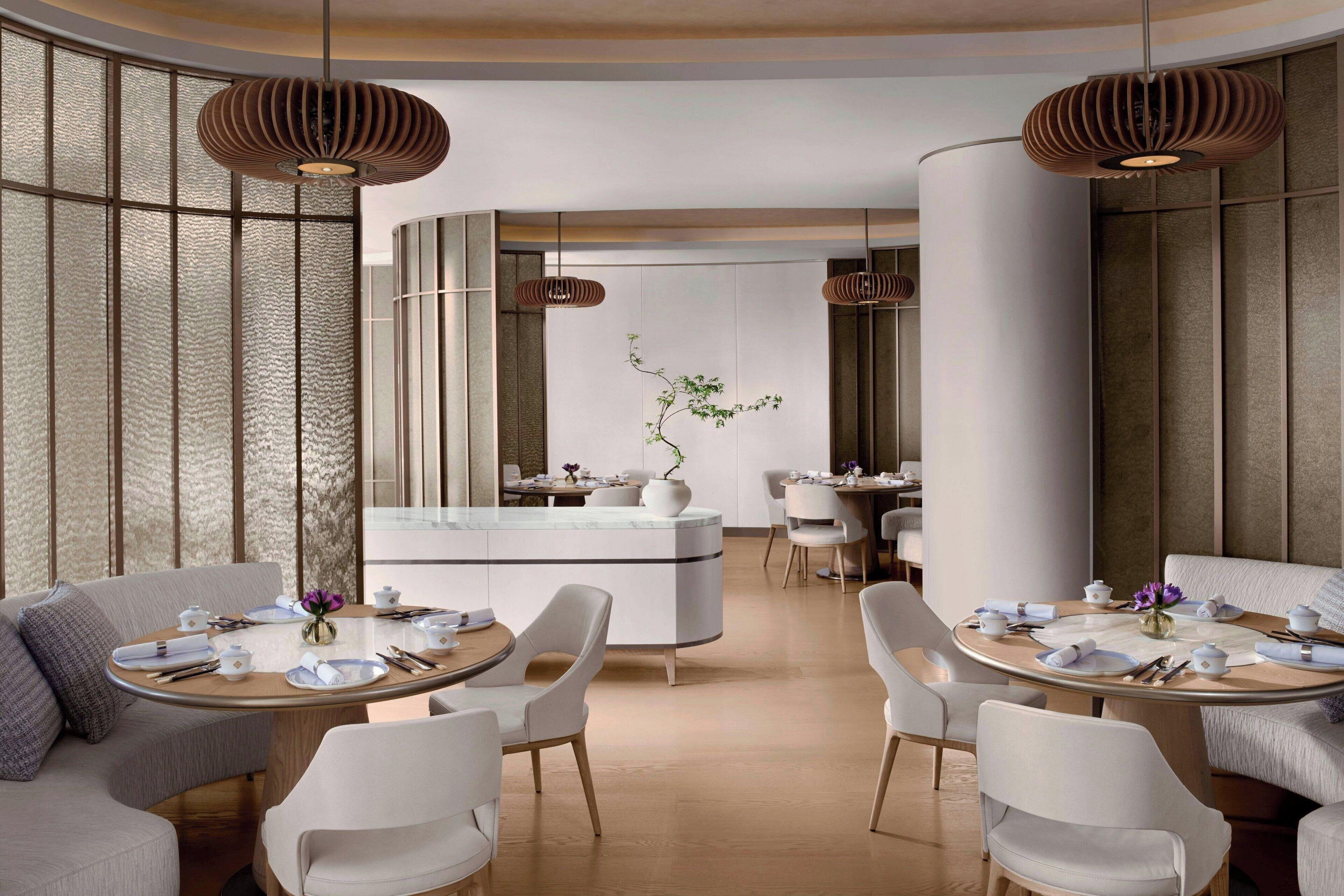 A modern dining area with round tables, white chairs, and hanging pendant lights.