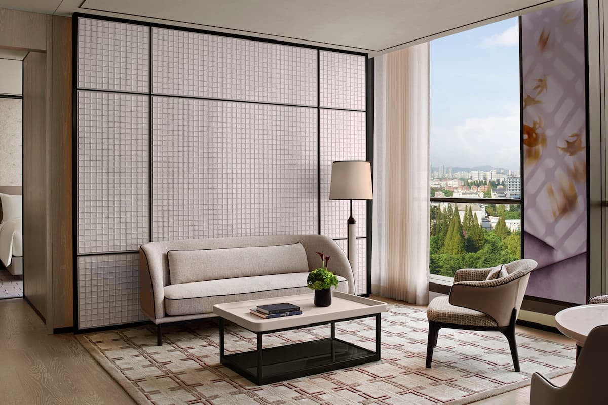 A modern living room with a sofa, a coffee table, a chair, and a view of a cityscape through large windows.