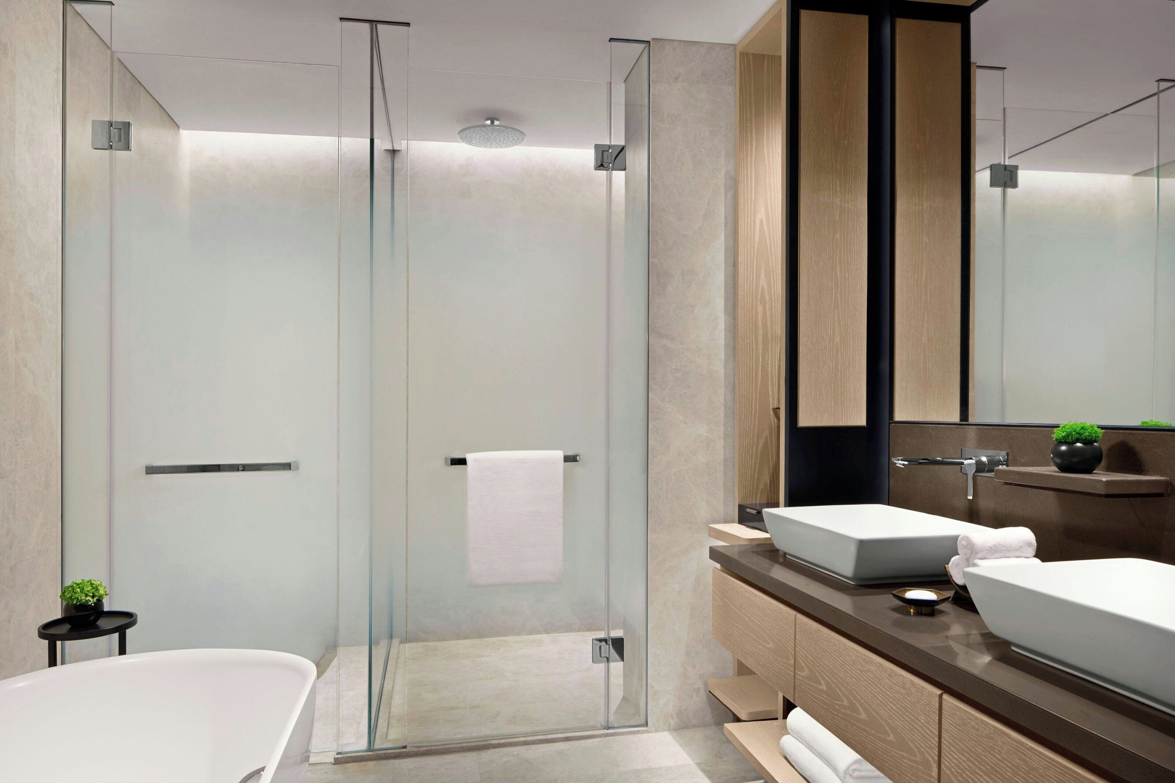 Un baño moderno con ducha de vidrio, dos lavamanos y un espejo grande.