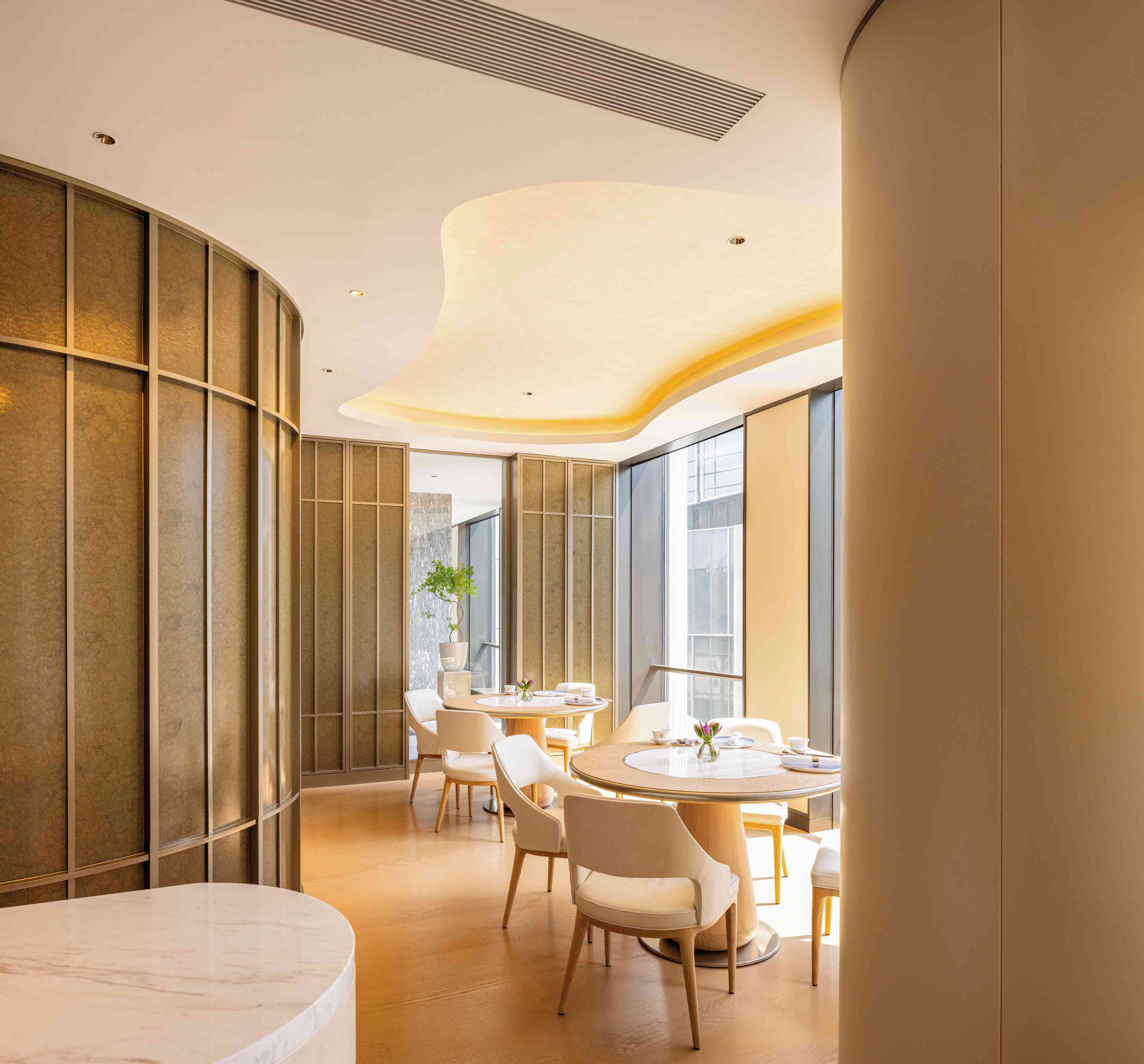 A modern dining area with a round table, white chairs, and a large window providing natural light.