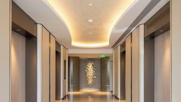 A modern hotel corridor with a curved ceiling, recessed lighting, and a reflective floor.