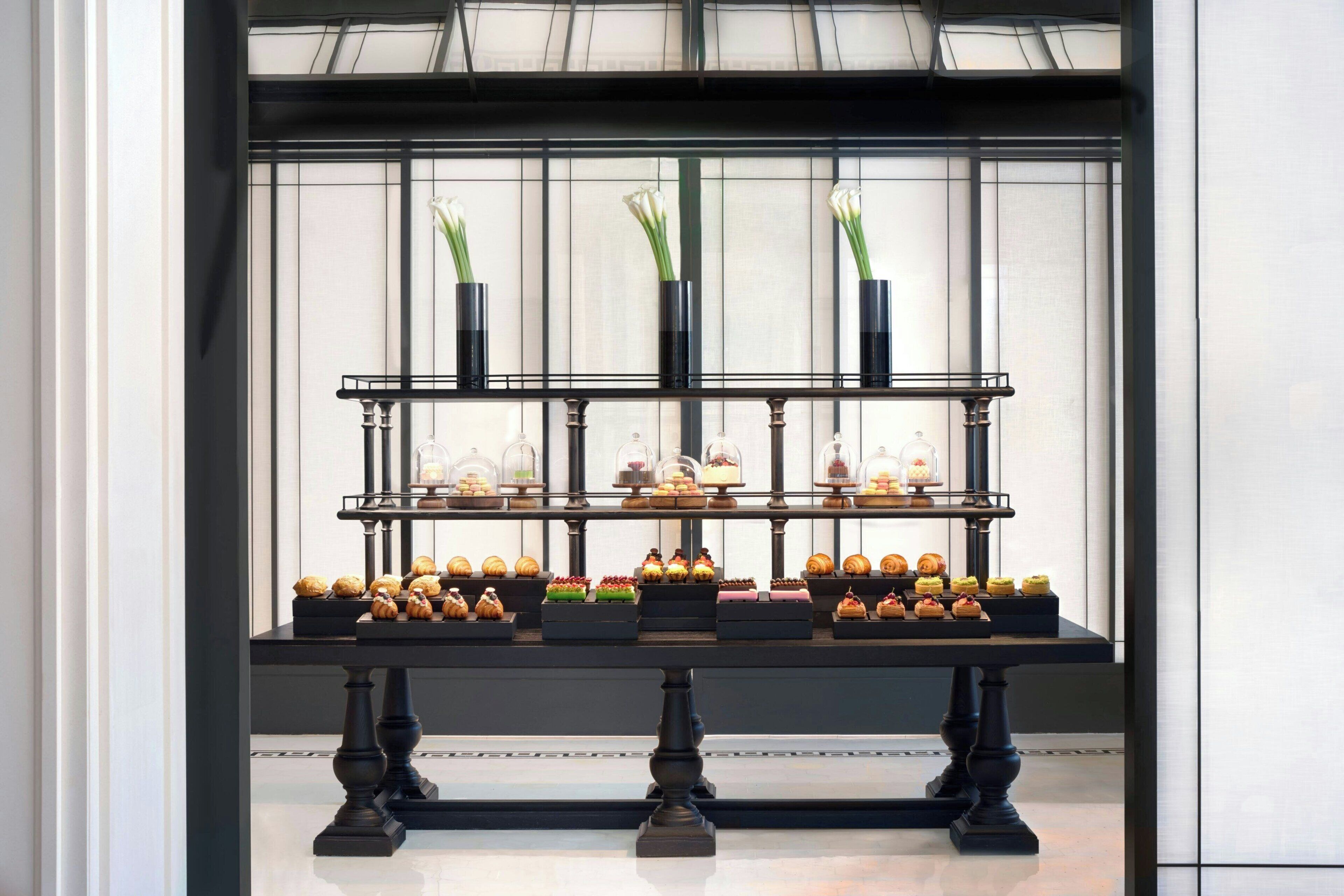 A display of pastries and flowers in front of a window with a black frame.