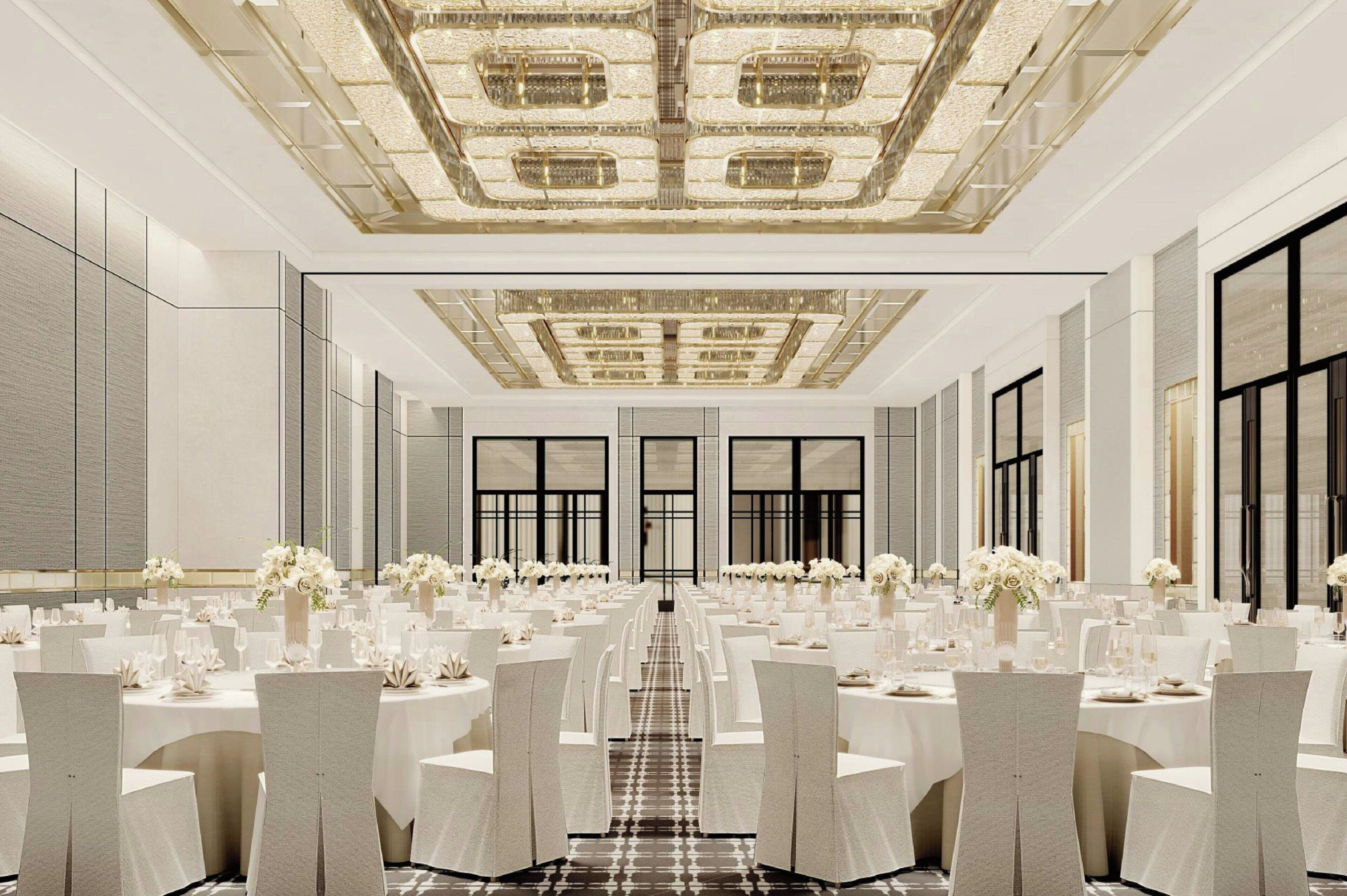 A banquet hall with long tables set for a formal event, featuring a central chandelier and a symmetrical layout.
