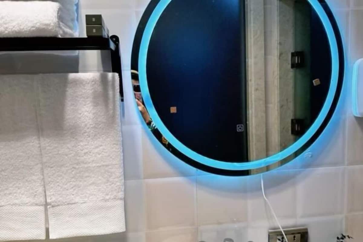 Une salle de bain avec un miroir rond, un porte-serviettes et une prise électrique visible.