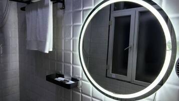 A bathroom with a round mirror, a towel rack, and a shelf with toiletries.