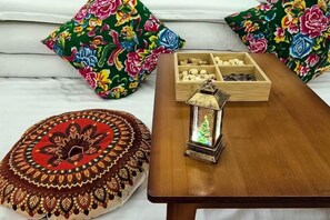A bed with colorful floral pillows, a wooden side table with a lantern, and a decorative box.