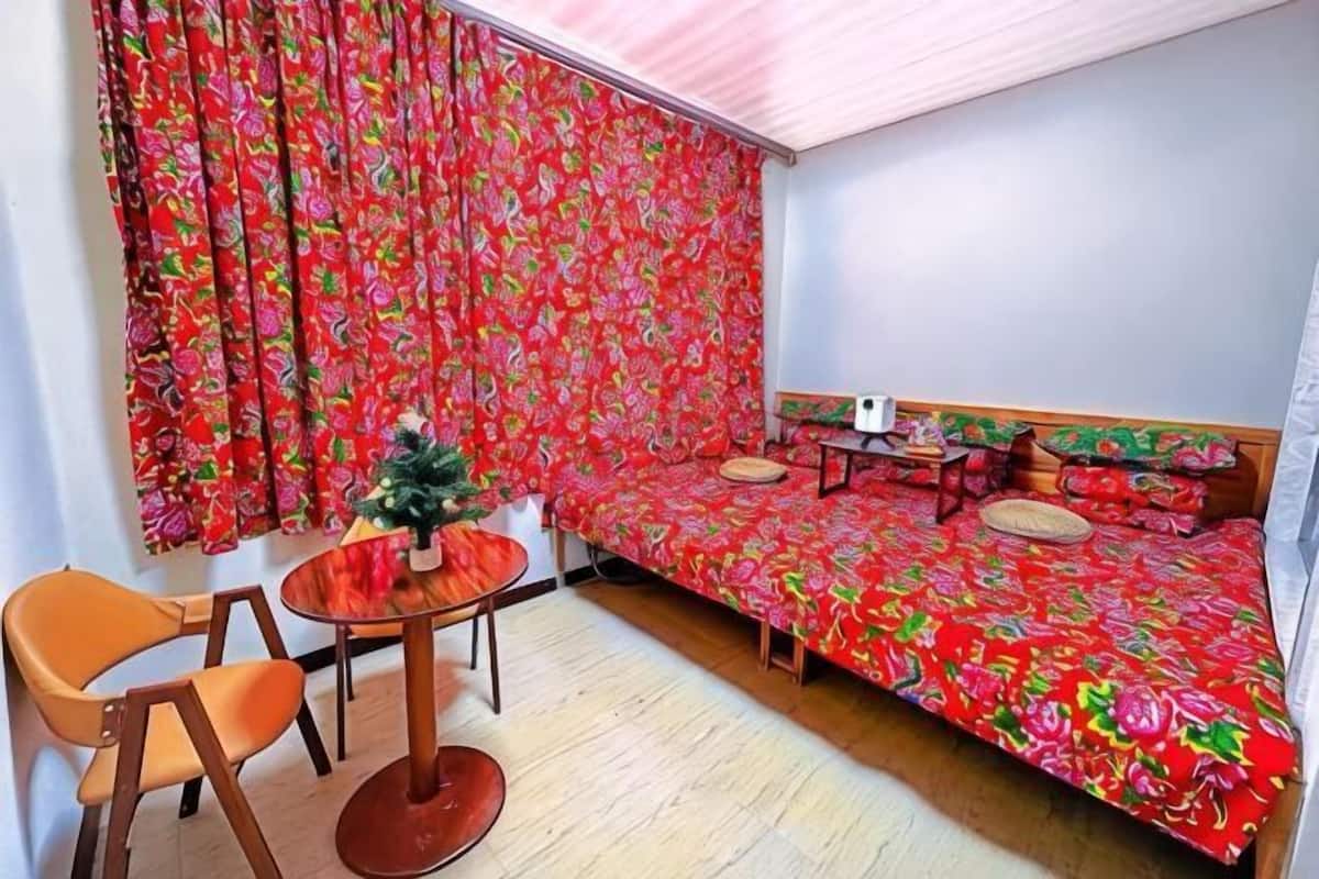 Une pièce avec un lit, une petite table, une chaise et un sapin de Noël.