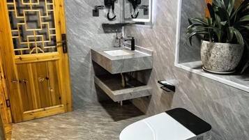 A bathroom with a wooden door, a marble sink, a mirror, a potted plant, and a toilet.