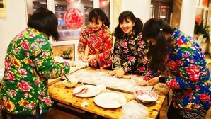 Un grupo de personas con vestimenta tradicional colaborando en una mesa con comida y utensilios.