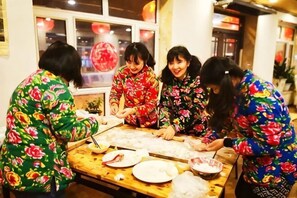 A group of people in traditional attire working together at a table with food items and utensils.