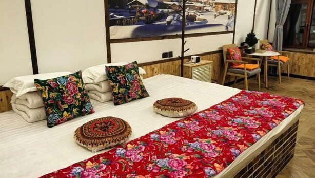 Una cama con ropa de cama floral, una ventana con vistas a un pueblo nevado y una pequeña mesa con sillas.