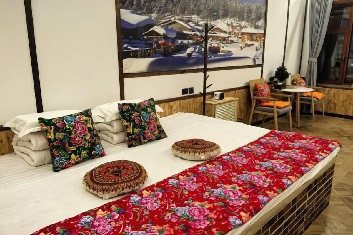 Un lit avec une literie à motifs floraux, une fenêtre donnant sur un village enneigé et une petite table avec des chaises.