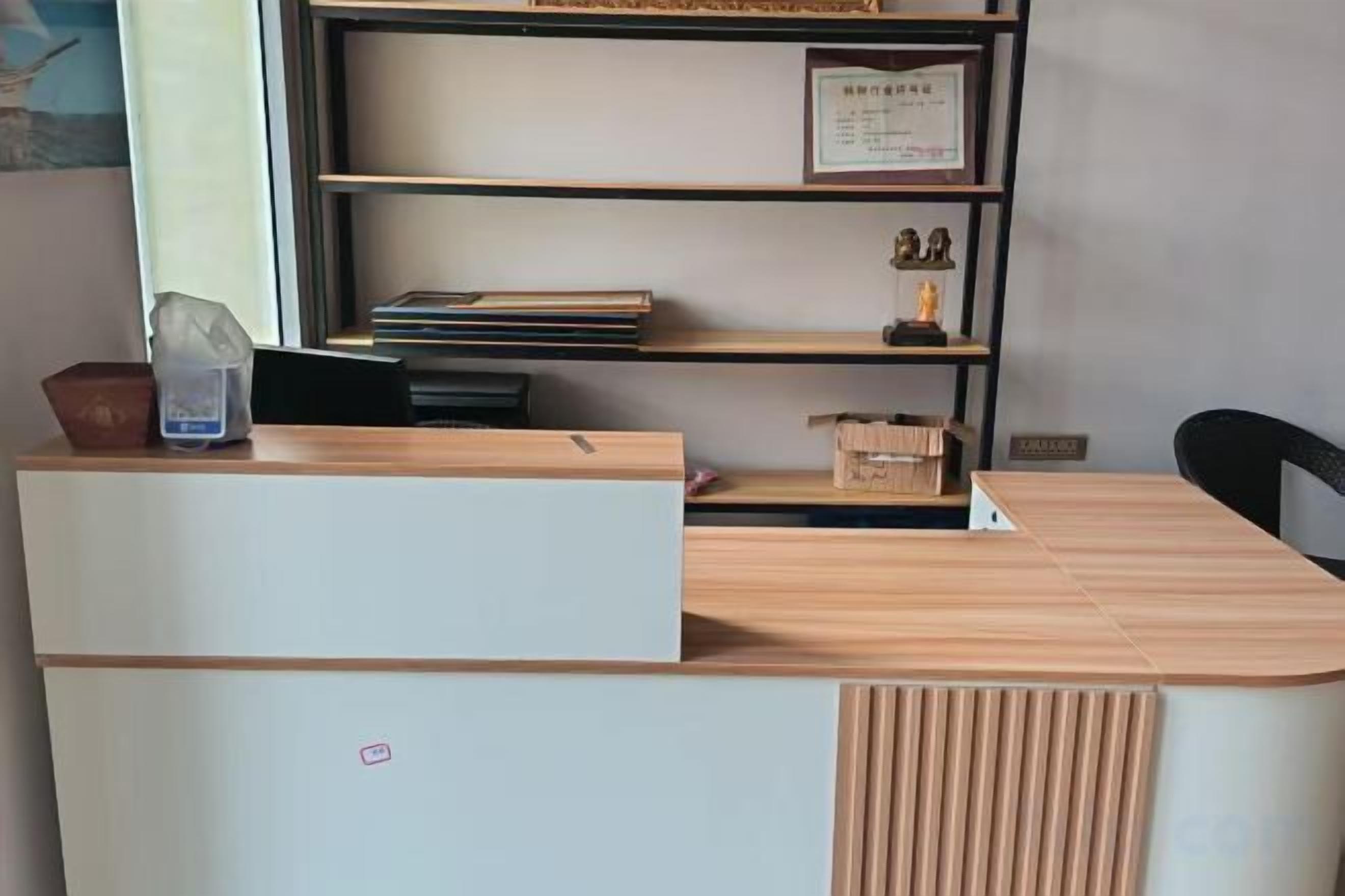 A reception desk with a white front panel, a wooden counter, and a shelf with books and a framed certificate.