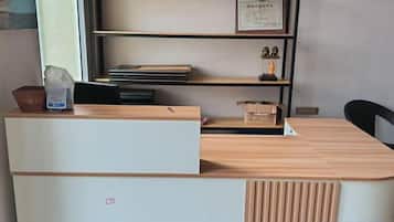 A reception desk with a white front panel, a wooden counter, and a shelf with books and a framed certificate.