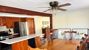 Una cocina con armarios de madera, un refrigerador de acero inoxidable, una estufa y un comedor con una mesa y sillas de madera.