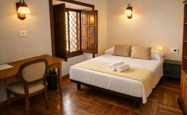 A hotel room with a wooden desk, a bed with white linens, two wall sconces, and a wooden wardrobe. - La Casona de Arona (Arona)