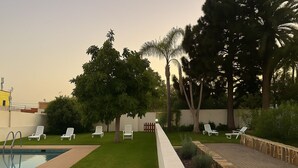 A pool area with lounge chairs, a well-maintained lawn, and tall trees. - La Casona de Arona (Arona)