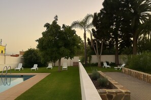 A pool area with lounge chairs, a well-maintained lawn, and tall trees. - La Casona de Arona (Arona)