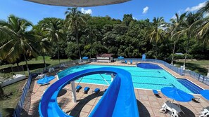 Una amplia piscina exterior con varias pistas de natación, rodeada de palmeras y con sombrillas.