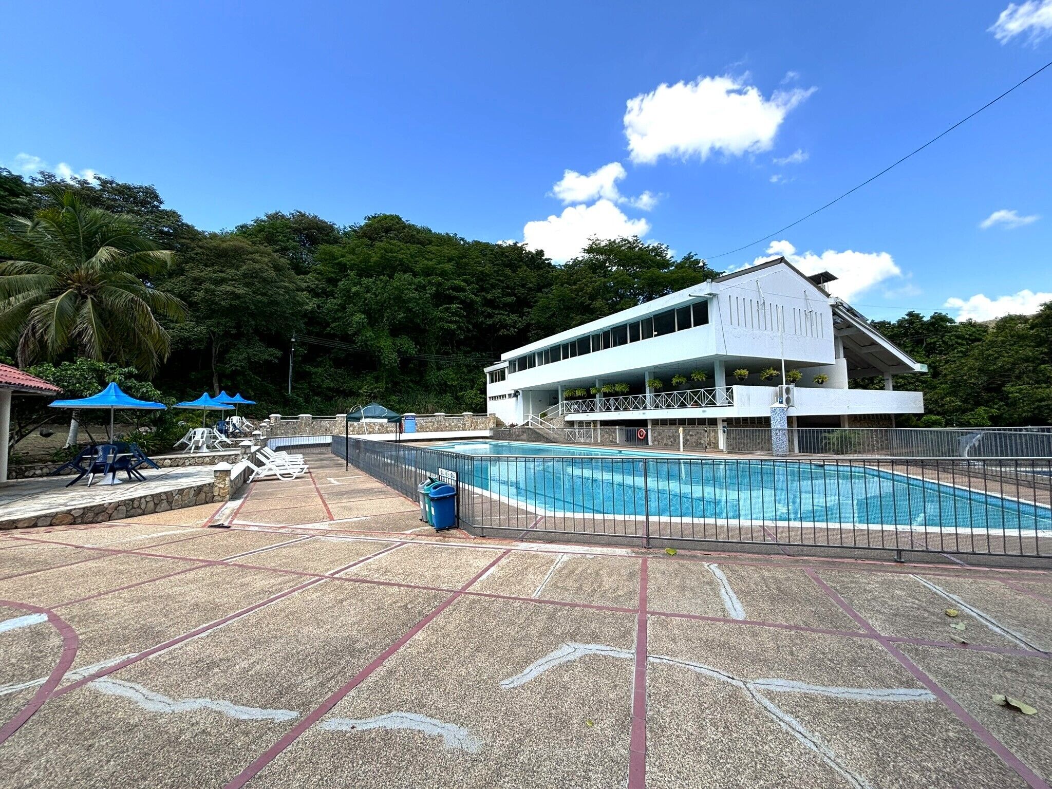 A pool area with lounge chairs and umbrellas, a building with a balcony, and a clear blue sky.