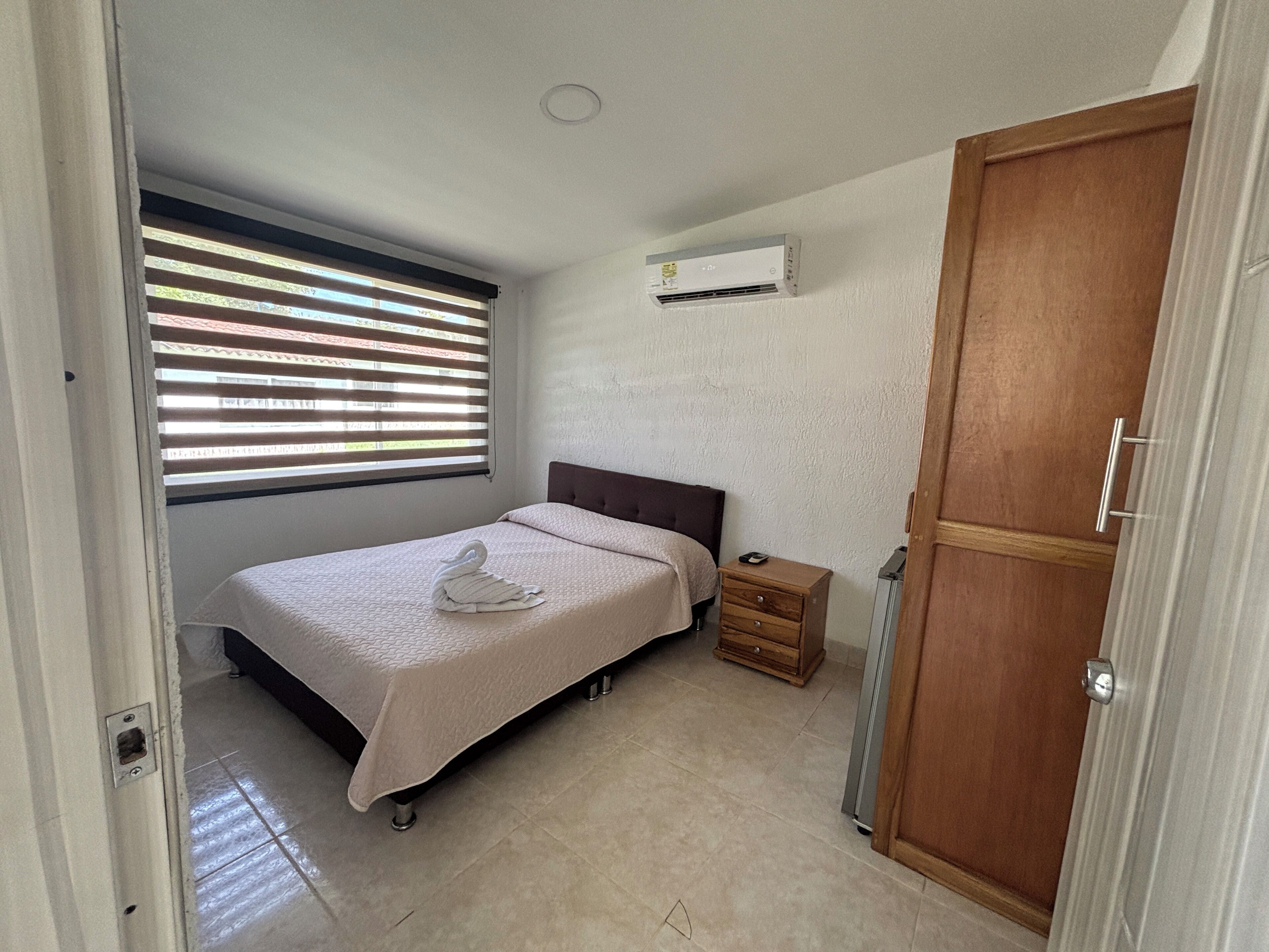 Un dormitorio con cama, mesita de noche, armario y ventana con persianas.