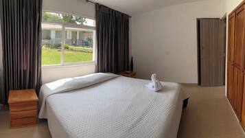 A hotel room with a bed, a wooden nightstand, a window with curtains, a wardrobe, and a view of the outside.