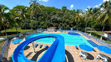 Relax by the pool surrounded by lounge chairs and umbrellas, with a clear water slide and lush greenery.