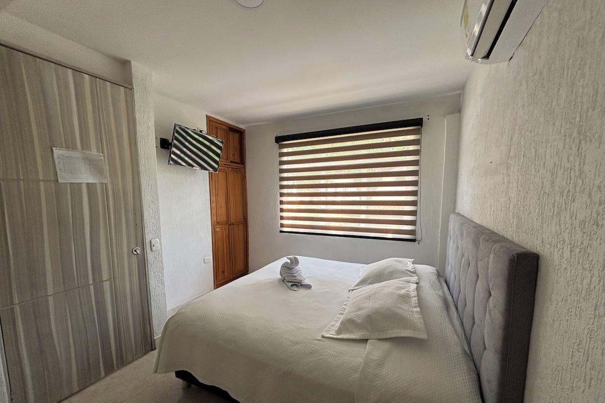 Un dormitorio con cama, armario, ventana con persianas y ventilador de techo.