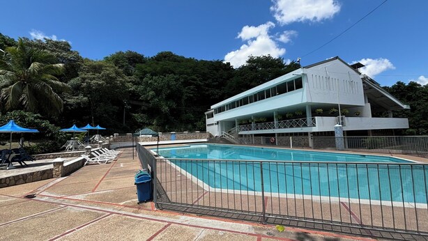 Una piscina con un edificio blanco al fondo, rodeada de árboles.