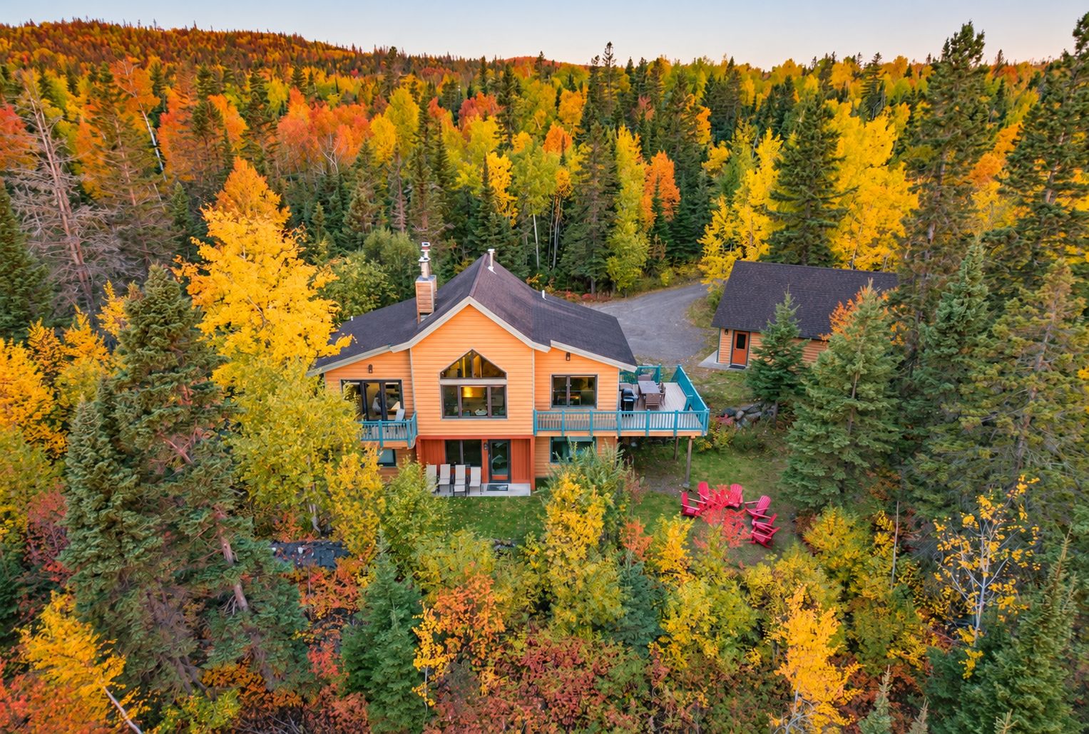Una casa de dos pisos con balcón, rodeada por un bosque con follaje otoñal.