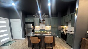 A modern kitchen with a central island, two bar stools, and a stainless steel refrigerator. - Cozy cabin in lovely Longview with WiFi, AC (Longview)