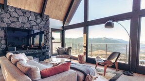 A modern living room with a stone wall, a large flat-screen TV, a sofa, a coffee table, and a view of the ocean. - Breathtaking Designer A-Frame In The High Desert (Mountain Center)
