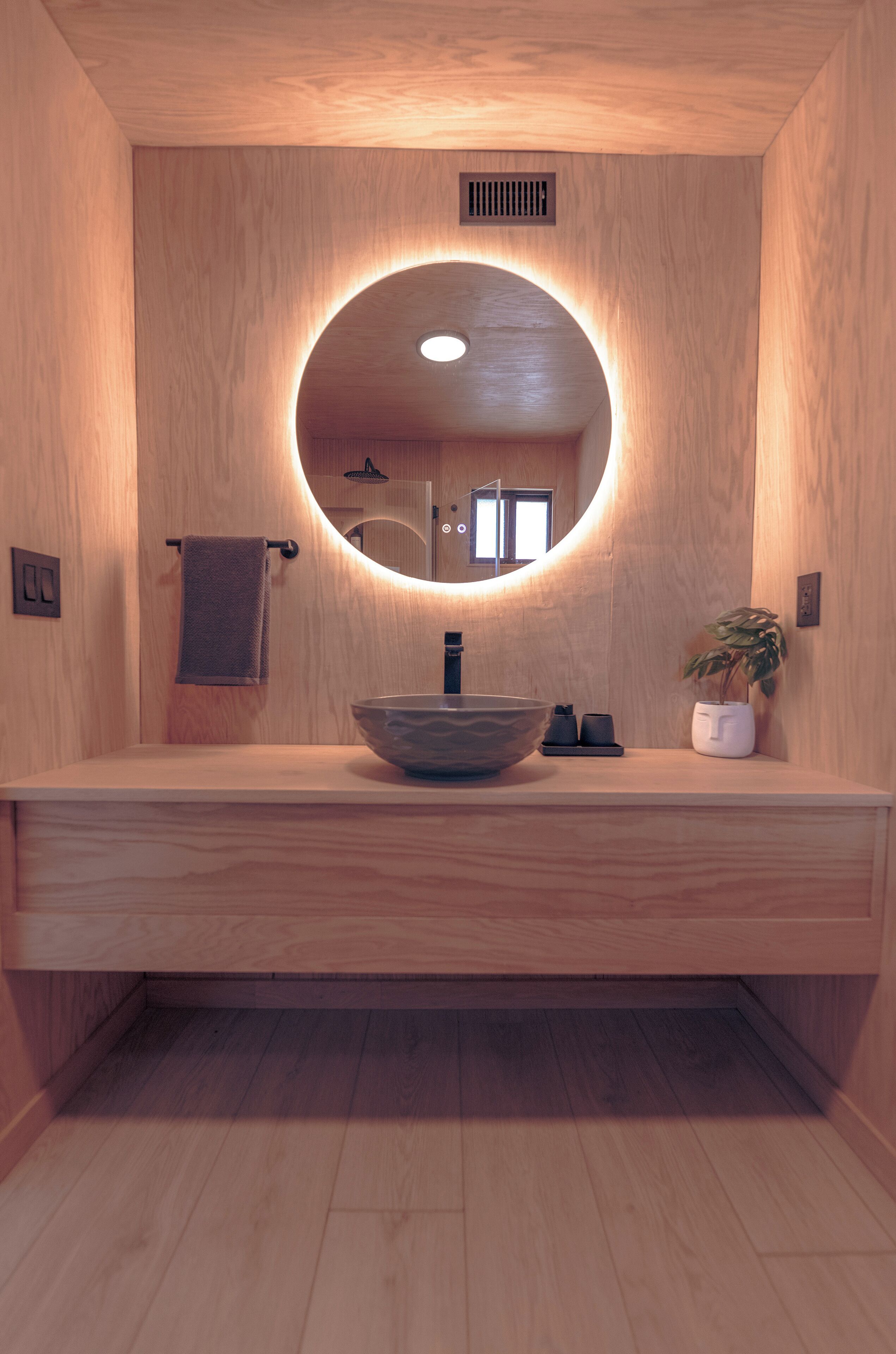Une salle de bain en bois avec un miroir rond, un lavabo et un porte-serviettes.