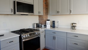 Een moderne keuken met grijze kastjes, een roestvrijstalen fornuis, een magnetron en een koffiezetapparaat.
