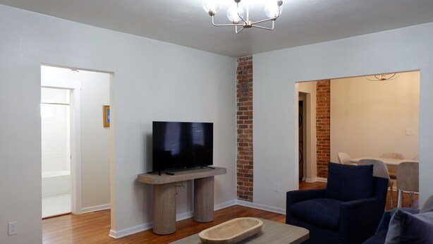 Een moderne woonkamer met een flatscreen televisie op een houten standaard, een donkerblauwe fauteuil en een klein houten tafeltje.