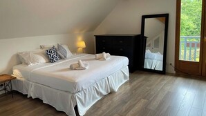 A bedroom with a large bed, a dresser, a mirror, and a window with a view of greenery.