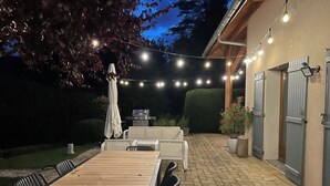 An outdoor patio with a wooden table and chairs, string lights, and a barbecue grill.