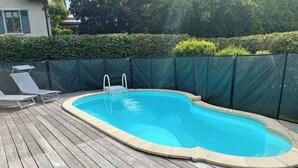 A rectangular swimming pool with a wooden deck, surrounded by a green fence.