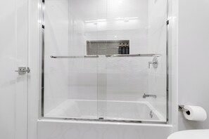 A modern bathroom with a glass-enclosed shower, a white bathtub, and a toilet.