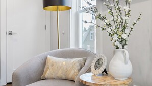 Un salon moderne avec un canapé gris, une petite table ronde ornée d’un vase blanc et d’un cadre photo, ainsi qu’une grande lampe sur pied.