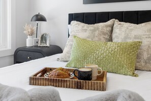 A neatly made bed with a tray of croissants and coffee, a black headboard, and decorative pillows.