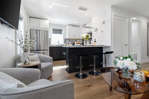 A modern kitchen with a central island, bar stools, and a dining area with a glass table. - Parking 3BR2Bth, Cambridge/Boston, W/D, Subway,A/C (Somerville)