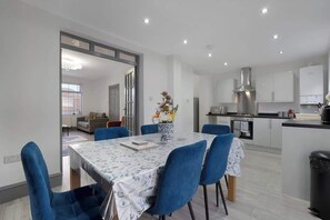 A modern kitchen with white cabinets, a stainless steel range hood, and a dining area with a table and blue chairs.