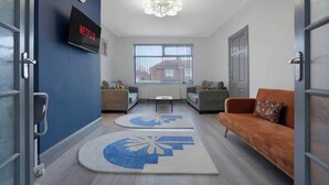 A modern living room with a TV, sofas, a coffee table, and large windows.