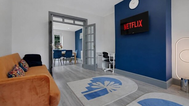 A modern living room with a blue accent wall, a Netflix sign, a sofa, and a dining area in the background.