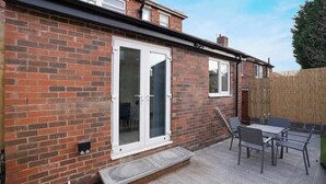 A brick house with a white-framed sliding door, a patio with a table and chairs, and a wooden fence.