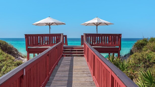 A wooden walkway leading to beach umbrellas, with clear blue ocean views.