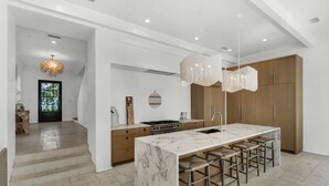 A modern kitchen with a marble island, wooden cabinets, and a hanging light fixture.